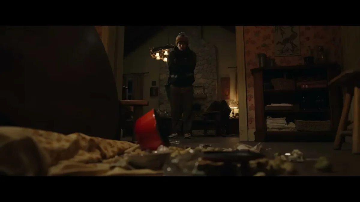 A man in a knit hat sits in a dim, lamplit room in a scene from Resident Evil (2026)