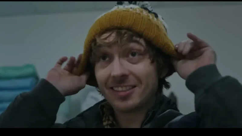 A young man in a yellow knit beanie smiles at the camera in a scene from the 2026 film Resident Evil