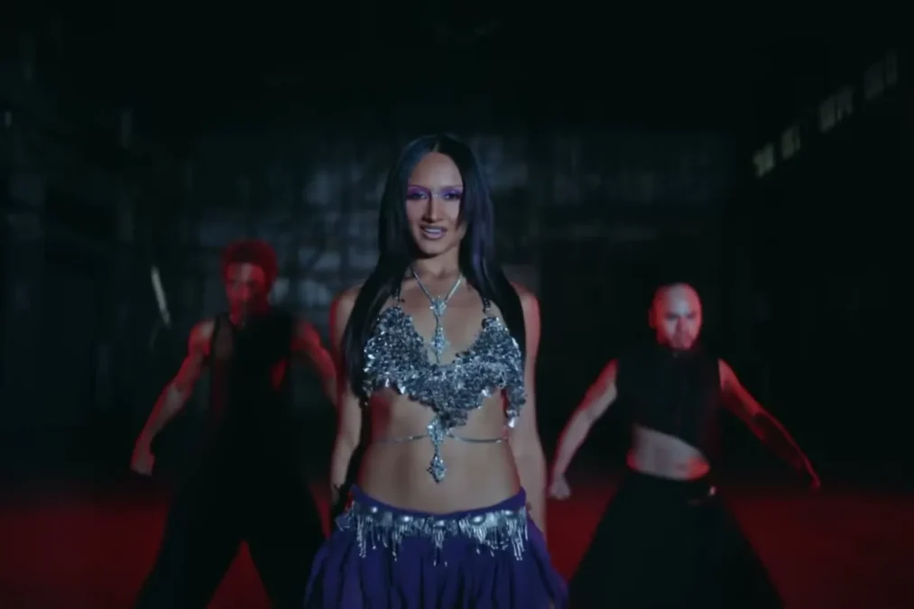 Rhea Raj in a jeweled silver top and blue skirt dancing with a crew in a dark warehouse in the Killer music video