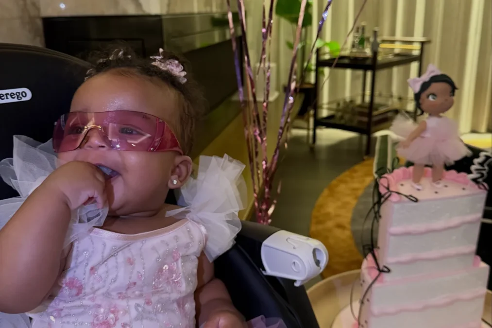 Rocki Irish Mayers in a pink tulle dress and pink sunglasses sitting beside a three-tier pink cake topped with a ballerina doll