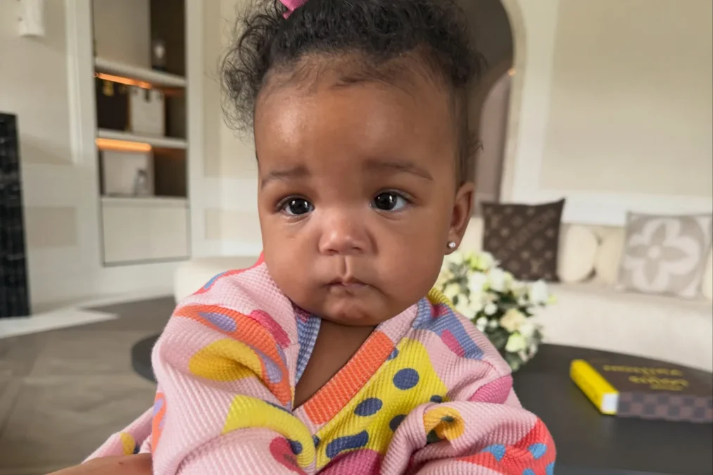 Baby Rocki in a colorful knit cardigan with polka dots, sitting on an adult's lap in a living room