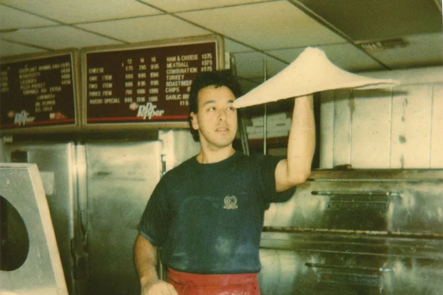Anthony Russo at 17 tossing pizza dough overhead in a pizzeria kitchen, in a family photo from Russo's New York Pizzeria