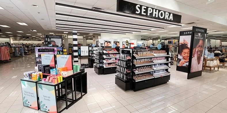 A Sephora at Kohl's shop inside a Kohl's department store: a black Sephora sign over makeup counters, fragrance value-set displays and posters