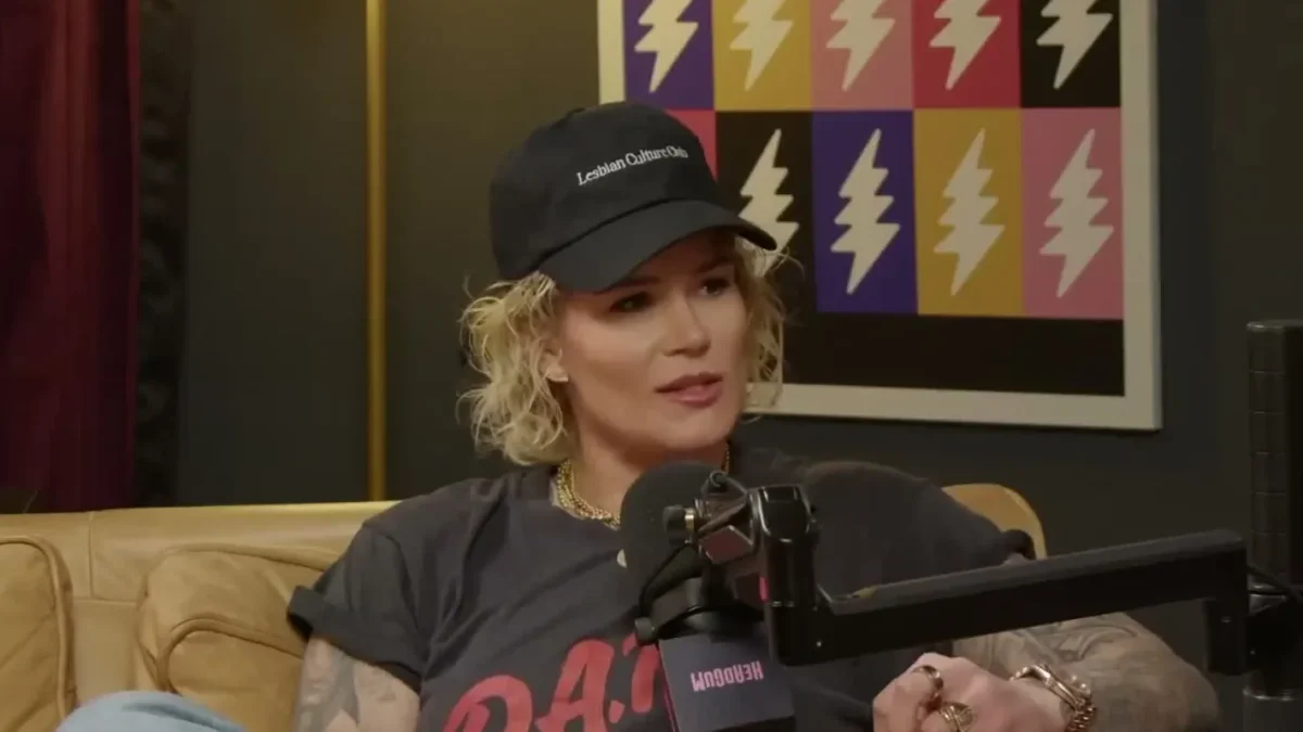 Ashlyn Harris in a black cap and gray T-shirt sitting on a tan couch at a podcast studio