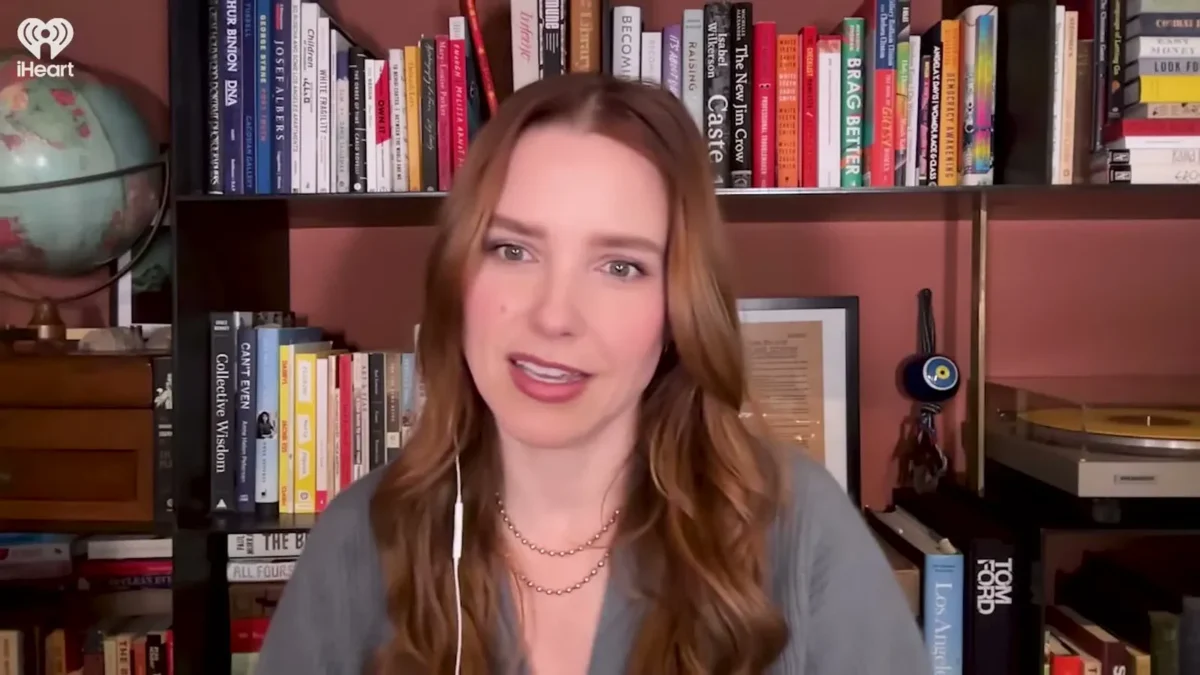 Sophia Bush with long wavy hair speaking on a video call in front of a bookshelf