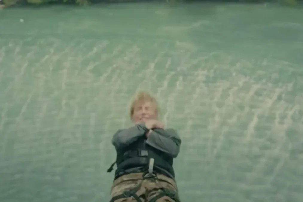 A Special Forces recruit falling backward toward a green lake with arms crossed over the chest, seen from above