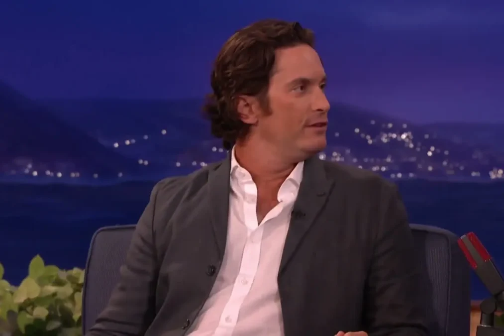 Oliver Hudson in a dark blazer and white shirt on the Conan talk show set