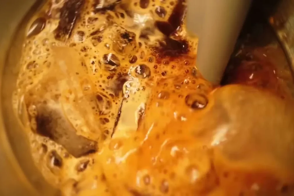 Espresso and ice cubes foaming under a steam wand in a steel pitcher, the step that aerates an Aerocano, in a Starbucks Korea commercial