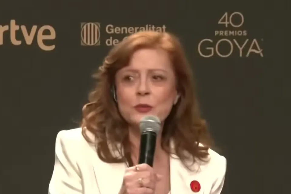 Susan Sarandon in a white suit holding a microphone at a press conference for the Goya Awards