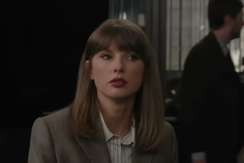 Taylor Swift in a brown blazer and striped shirt in a police squad room set during the SVU sketch