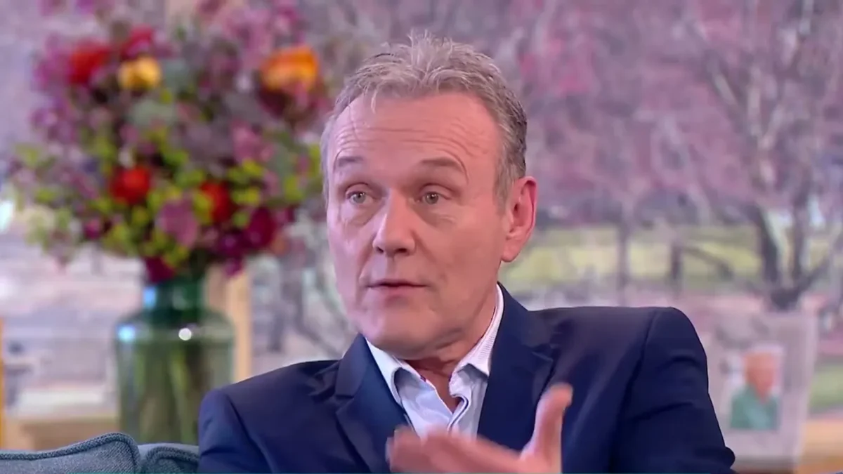 Anthony Head in a navy blazer talking on the This Morning sofa with flowers behind him