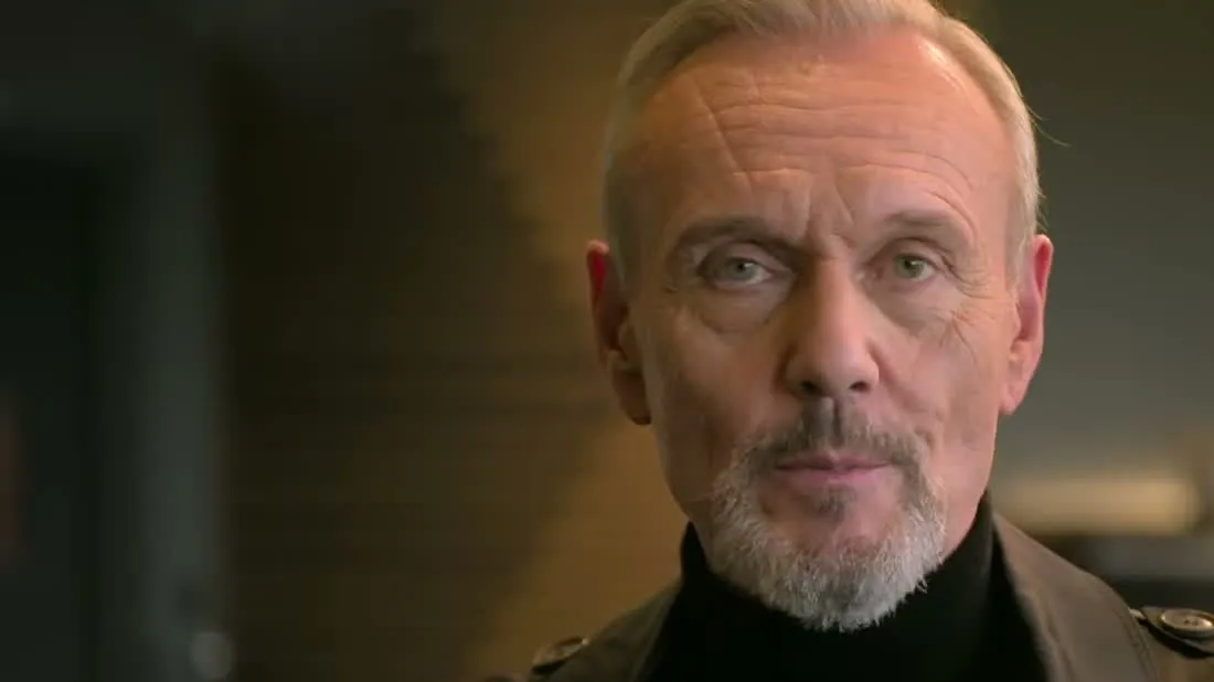 Anthony Head with short gray hair and a white beard in a black turtleneck during an interview