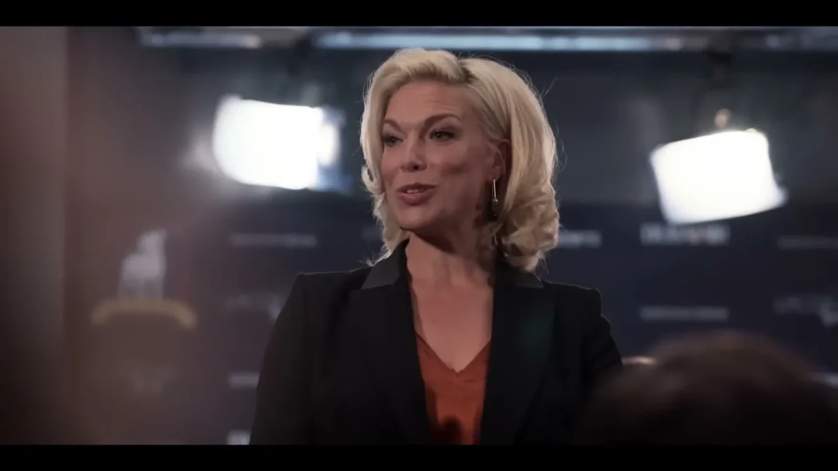 Hannah Waddingham as Rebecca Welton in a black blazer at a press conference in Ted Lasso