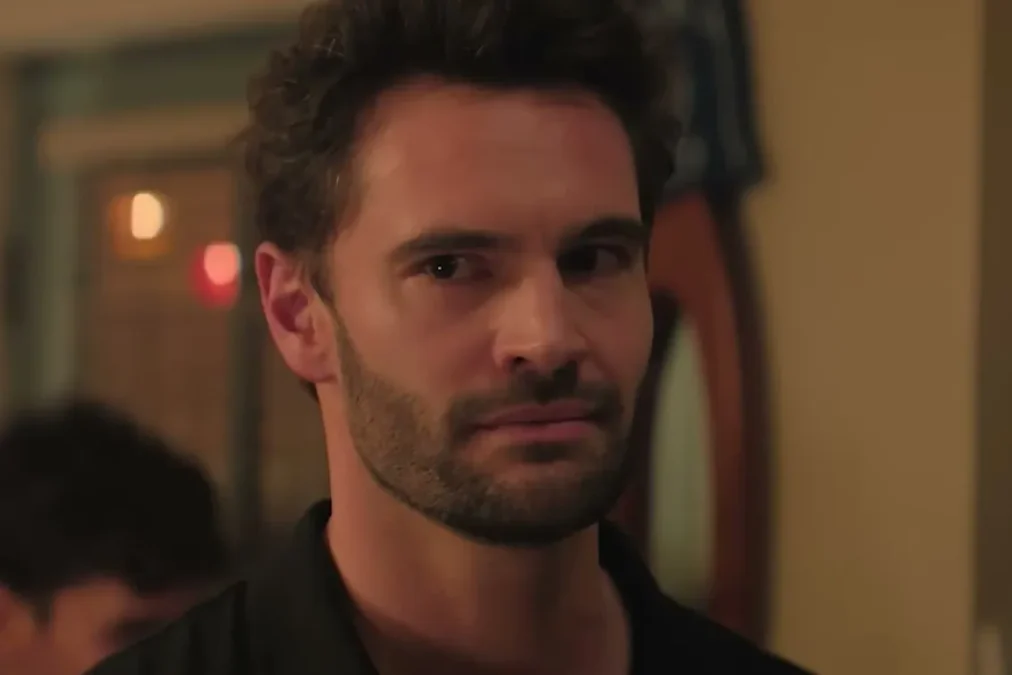 Tom Bateman as Adam Carlsen looking across a room at a party in The Love Hypothesis