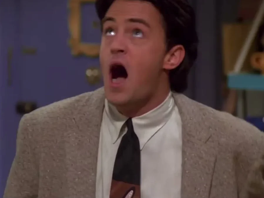Matthew Perry as Chandler Bing in a tweed jacket, mouth wide open and eyes rolled upward in the Friends apartment