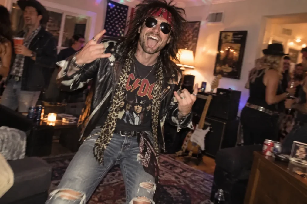 Illustration of a man dressed as an '80s rock star in a leather jacket, band T-shirt, leopard scarf, red bandana, aviators and ripped jeans at a house party