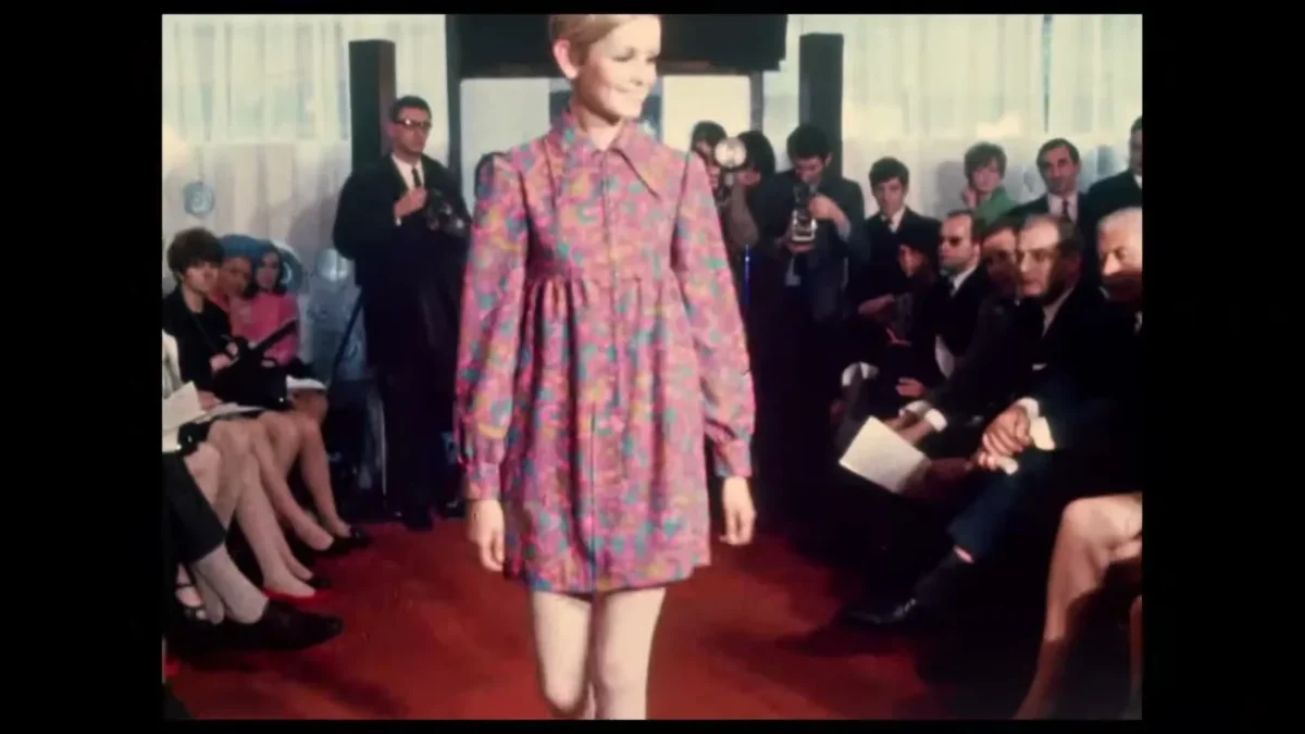 Archival footage of a 1960s fashion show with a model on a runway, from the documentary Twiggy