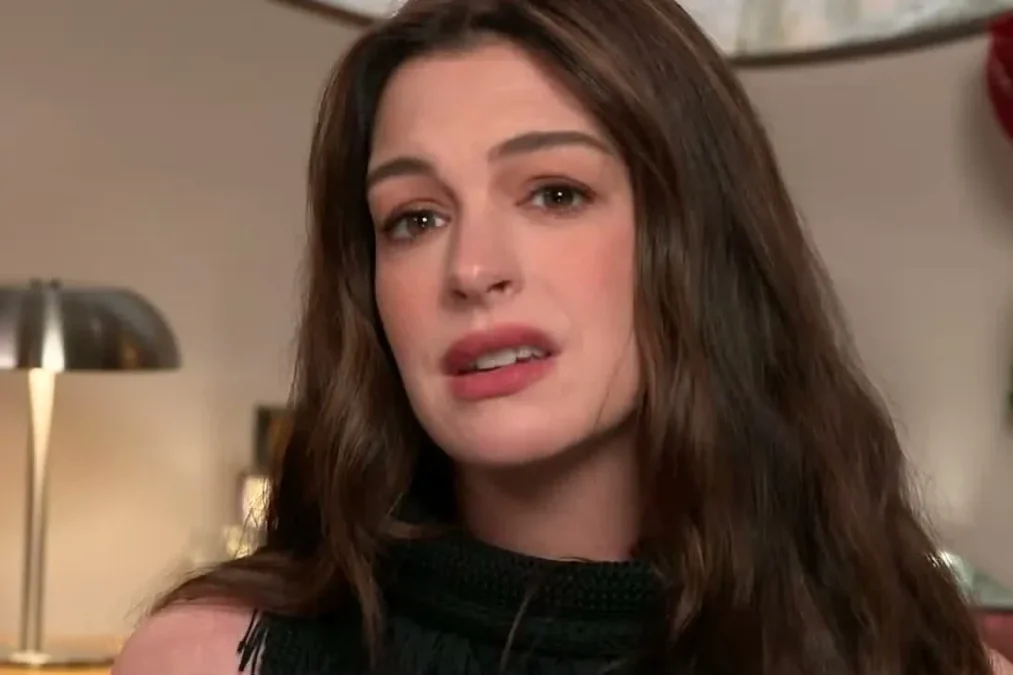 Anne Hathaway with long brown hair speaking during a TV interview