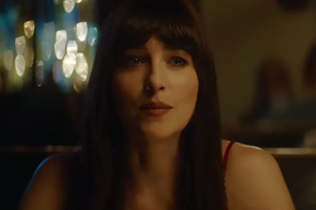 Dakota Johnson with dark bangs sitting in a dimly lit bar in a scene from Verity