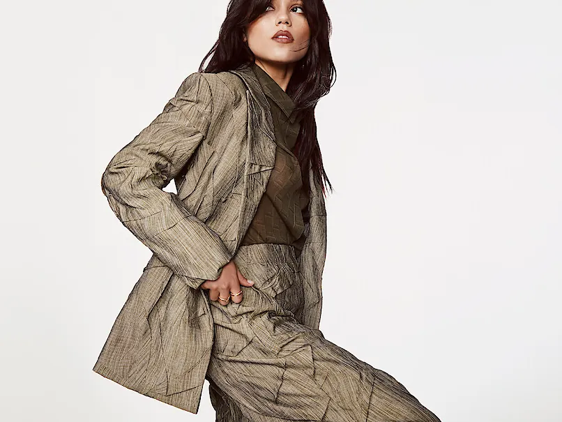 Jenna Ortega in a crinkled taupe suit posing against a white background