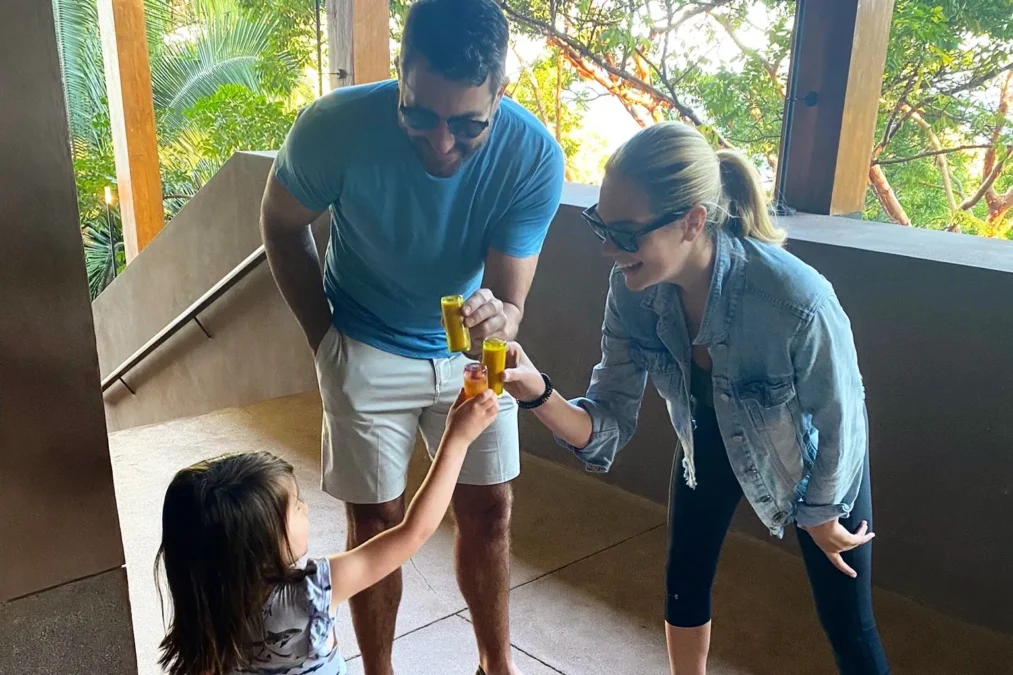 Justin Verlander and Kate Upton, both in sunglasses, toast with small wellness shots with their young daughter Genevieve under a covered patio