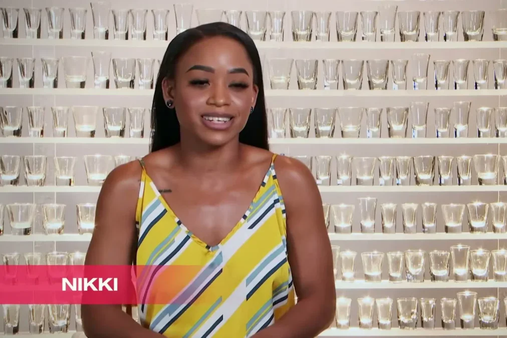 Nikki Hall in a yellow striped dress smiling in her Double Shot at Love confessional, with a name caption reading Nikki