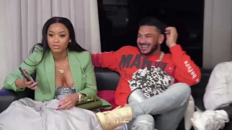 Nikki Hall in a green blazer and Pauly D in a red sweatshirt sit together on a black couch on Jersey Shore: Family Vacation