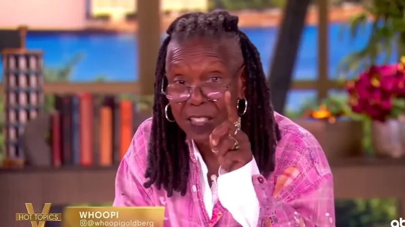 Whoopi Goldberg at the Hot Topics table on The View, in a pink jacket, pointing as she speaks