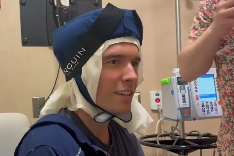 Will Reeve smiling in a blue cold cap strapped under his chin during chemotherapy, next to an infusion pump