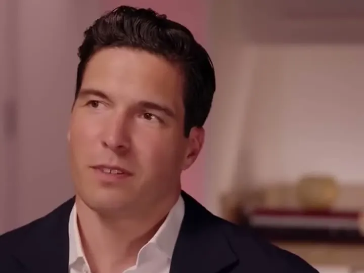 Will Reeve in a navy blazer and white shirt, listening during an interview