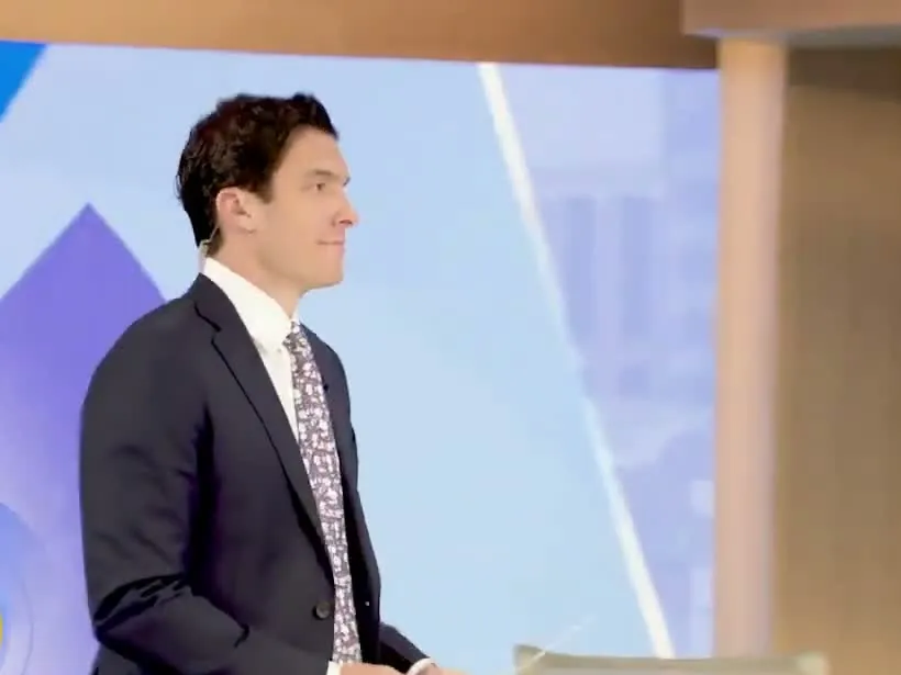 Will Reeve in a navy suit and floral tie standing on the Good Morning America set