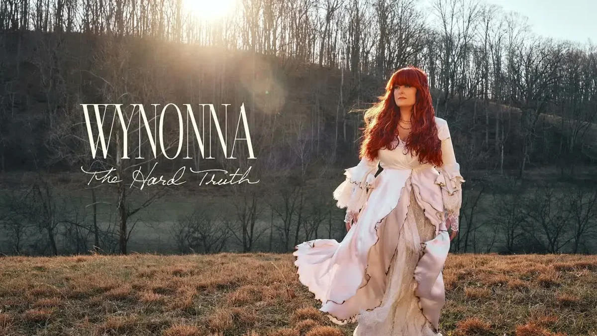 Wynonna in a long white dress walking through a winter field with the words Wynonna The Hard Truth