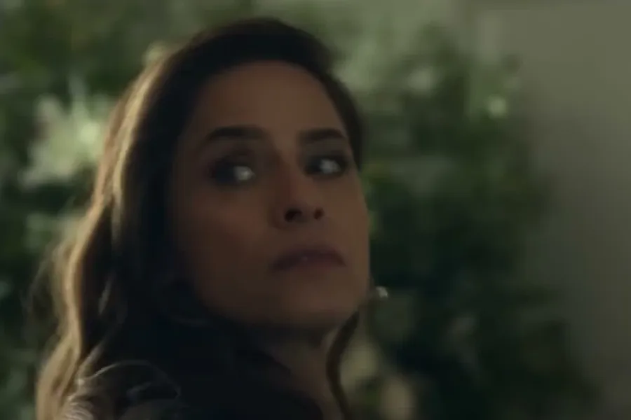 Amanda Peet as her character in the trailer for Your Friends & Neighbors, looking over her shoulder in a dim garden
