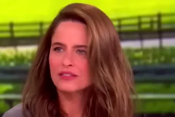 Amanda Peet with long wavy brown hair in a gray top talking on the set of The View
