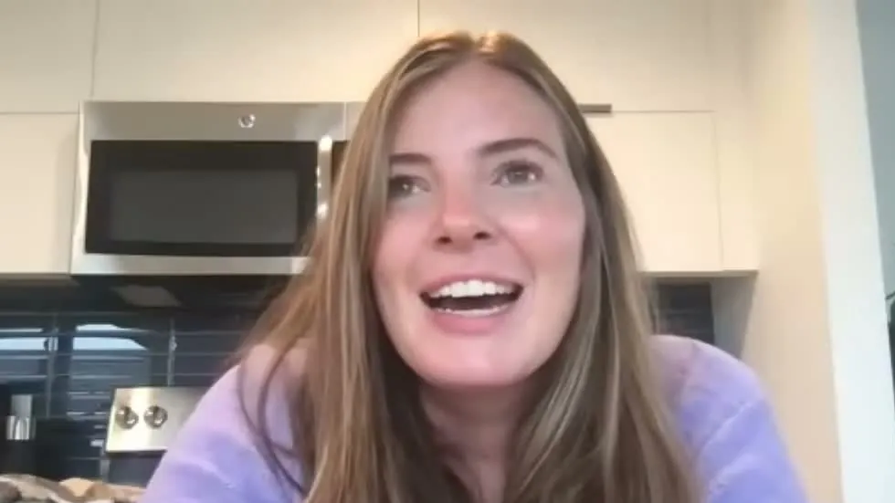 Brooke Eby in a lavender sweater smiling during a podcast video call in her kitchen