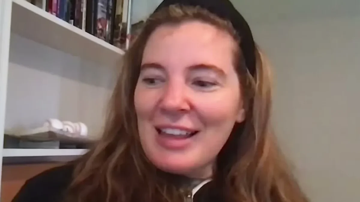 Brooke Eby in a black headband and jacket smiling during a podcast video call