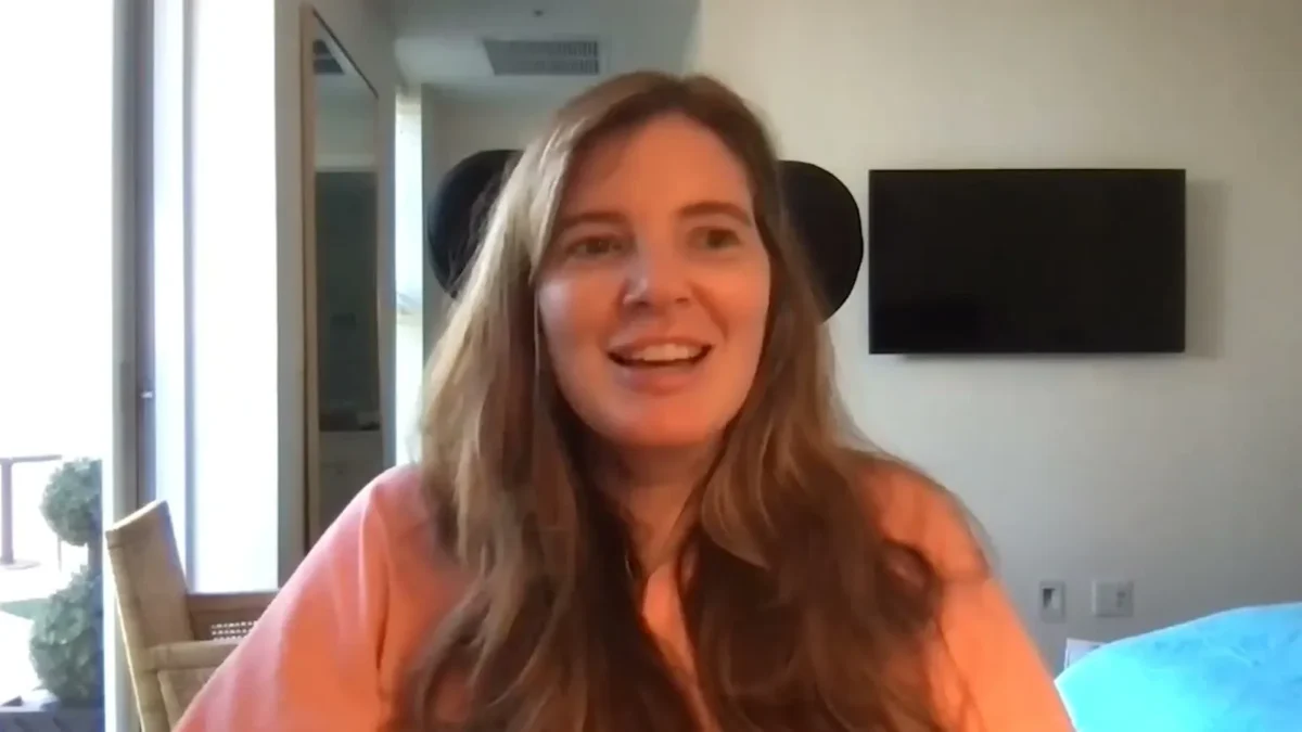Brooke Eby in an orange hoodie smiling during a podcast video call