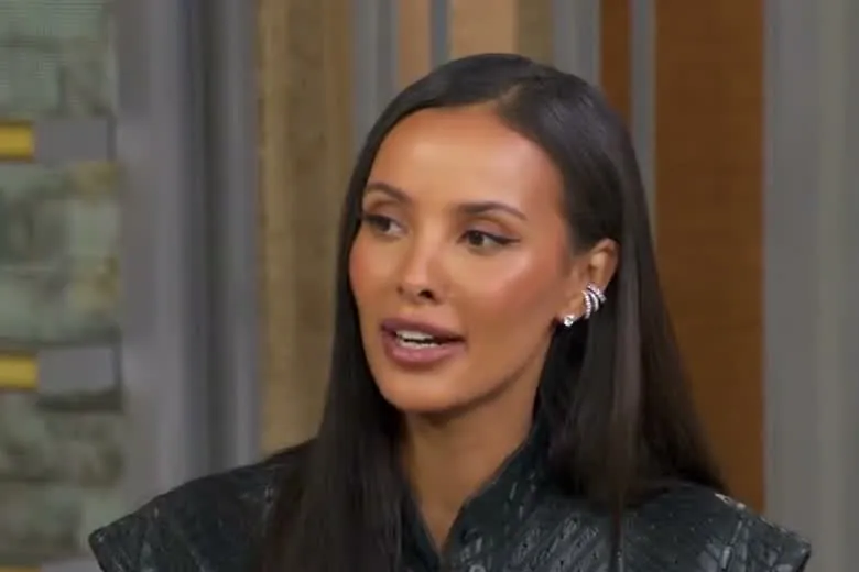 Maya Jama with long straight dark hair in a black leather top talking on the Good Morning America set