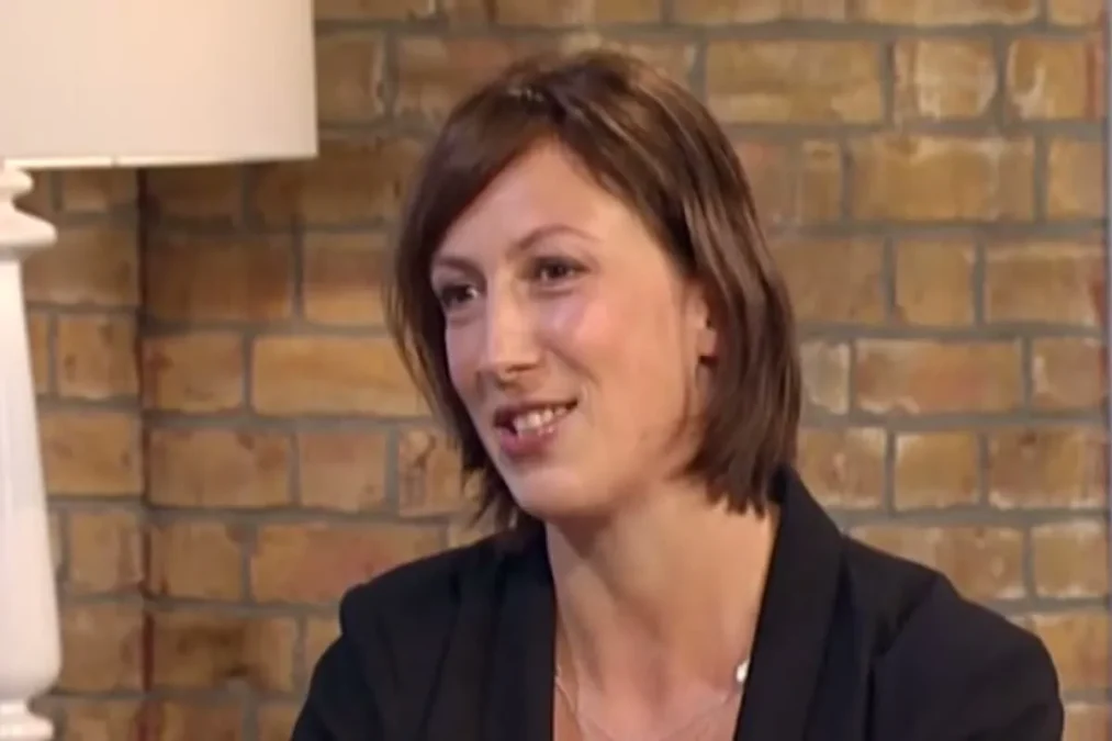 Miranda Hart with a brown bob and a black blazer smiling in front of a brick wall on the This Morning set