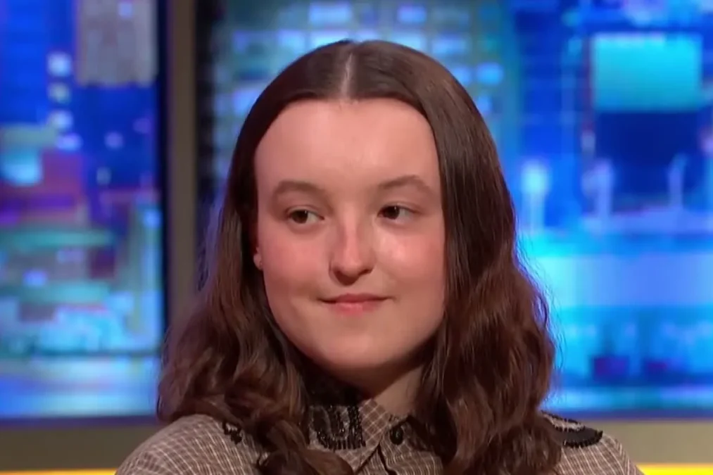 Bella Ramsey with long wavy brown hair in a patterned top on the set of The Jonathan Ross Show