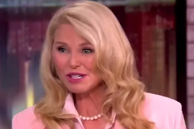 Christie Brinkley with long blond hair in a light pink blazer and pearl necklace talking on The View