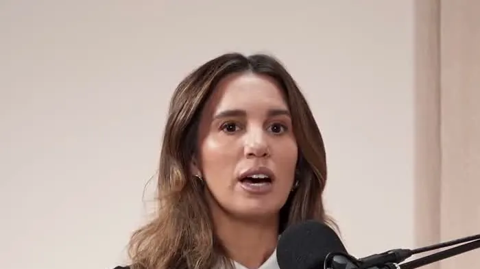 Christy Carlson Romano with shoulder-length brown hair speaking in front of a podcast microphone