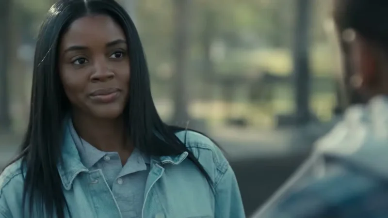 Naomi Baker as Anika, with long straight hair and a denim jacket, smiling at Jay Reeves as Carousel outdoors in Doing Life