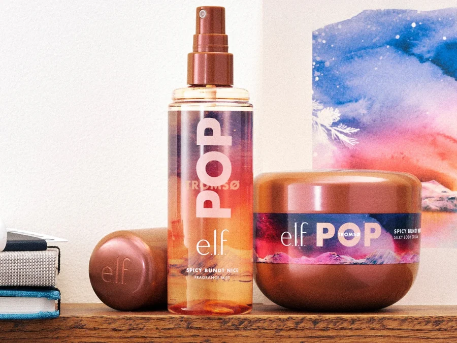The e.l.f. POP Spicy Bundt Nice fragrance mist and silky body cream on a wooden shelf in front of a watercolor painting of a snowy mountain