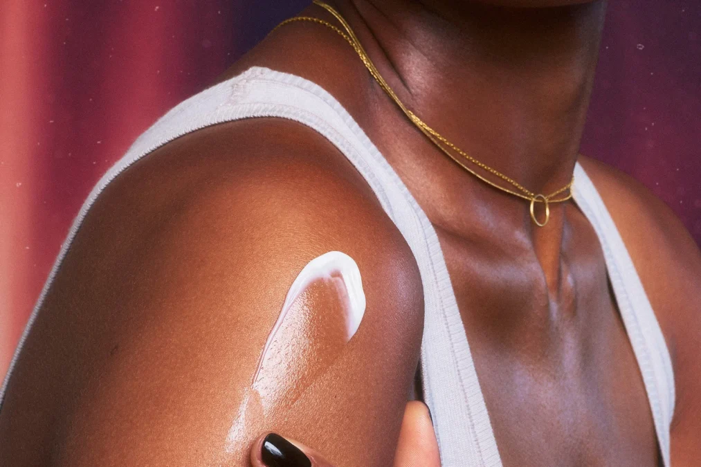 A woman in a white tank top with a swipe of e.l.f. POP silky body cream on her shoulder