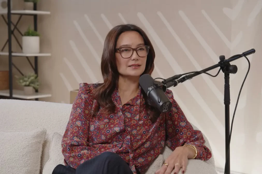 Emma Heming Willis in glasses and a patterned blouse seated by a microphone on a podcast set