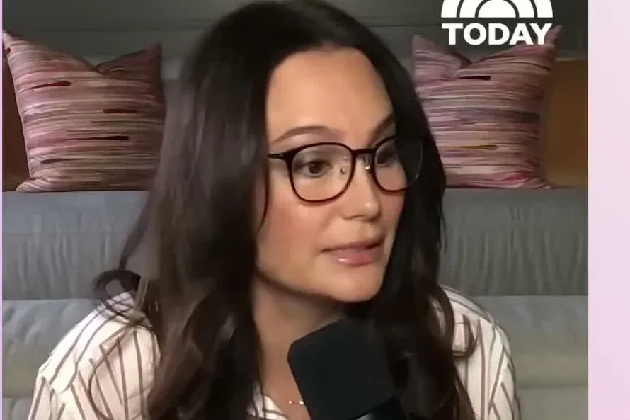 Emma Heming Willis in glasses and a striped shirt speaking into a microphone in a home setting