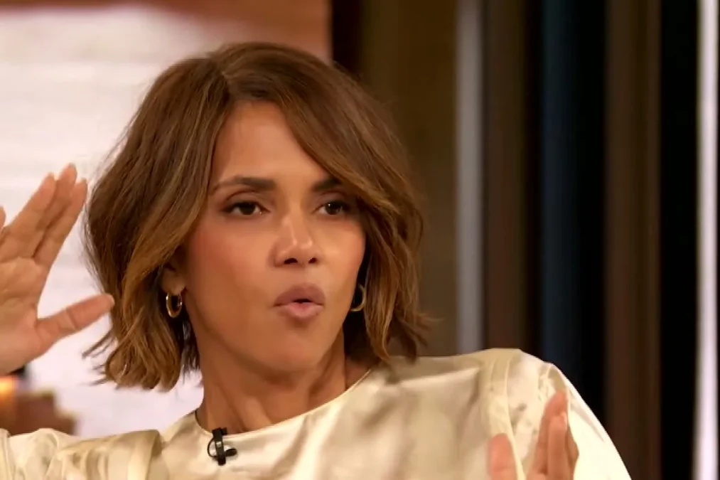 Halle Berry in a cream satin blouse with a short layered bob raising both hands while talking on The Drew Barrymore Show