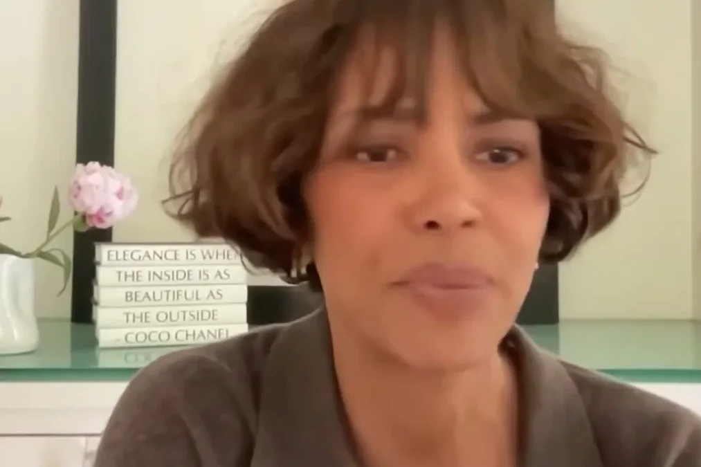 Halle Berry with a short bob and bangs talking on a video call with her hand raised on Hoda Kotb's podcast Making Space
