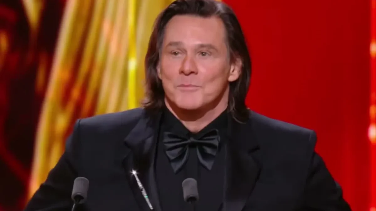 Jim Carrey in a black tuxedo and bow tie speaking at a podium with a gold César trophy in front of a red and gold backdrop